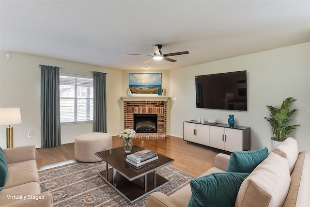 living area with ceiling fan, a brick fireplace, and wood finished floors