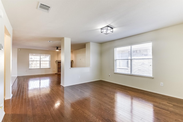 spare room featuring visible vents, a ceiling fan, dark wood-style floors, a fireplace, and baseboards