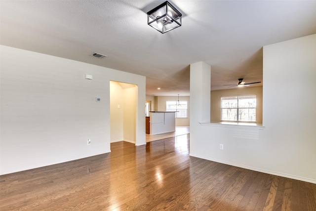 unfurnished living room with visible vents, ceiling fan with notable chandelier, baseboards, and wood finished floors