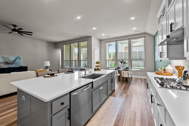 kitchen featuring under cabinet range hood, open floor plan, gray cabinets, stainless steel appliances, and a sink