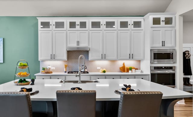 kitchen with decorative backsplash, a kitchen island with sink, a kitchen breakfast bar, white cabinetry, and appliances with stainless steel finishes