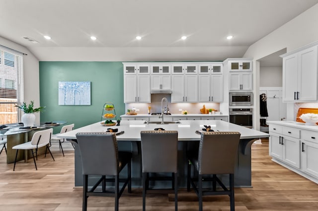 kitchen with a kitchen bar, stainless steel appliances, light countertops, and a kitchen island with sink