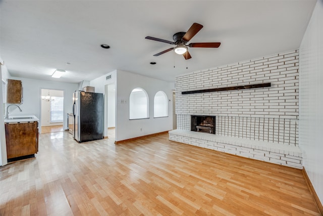 unfurnished living room with light hardwood / wood-style flooring, sink, ceiling fan with notable chandelier, and a brick fireplace