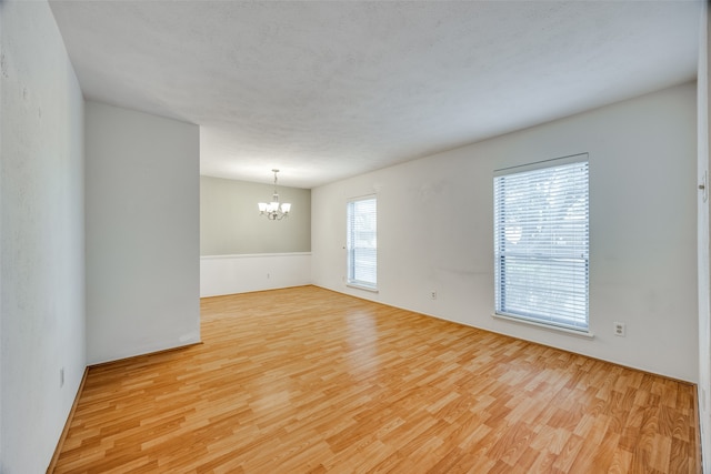 unfurnished room with a chandelier and light wood-type flooring