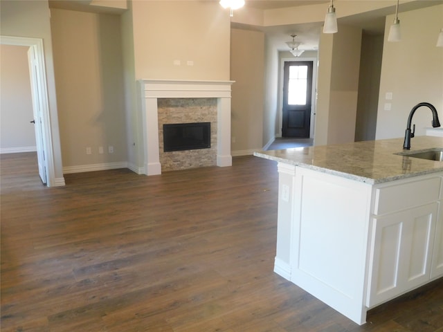 kitchen featuring hanging light fixtures, white cabinetry, light stone countertops, dark wood-type flooring, and sink