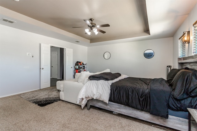 bedroom featuring carpet, a fireplace, a tray ceiling, and ceiling fan