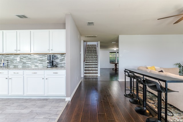 kitchen with light hardwood / wood-style flooring, white cabinets, light stone counters, and backsplash