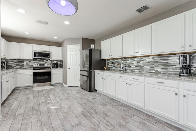 kitchen featuring white cabinets, stainless steel appliances, light wood-type flooring, and tasteful backsplash