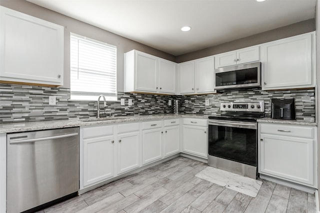 kitchen with stainless steel appliances, sink, light wood-type flooring, white cabinets, and light stone counters