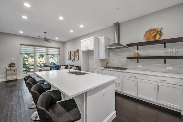 kitchen with a kitchen island with sink, wall chimney range hood, white cabinets, and dark hardwood / wood-style flooring