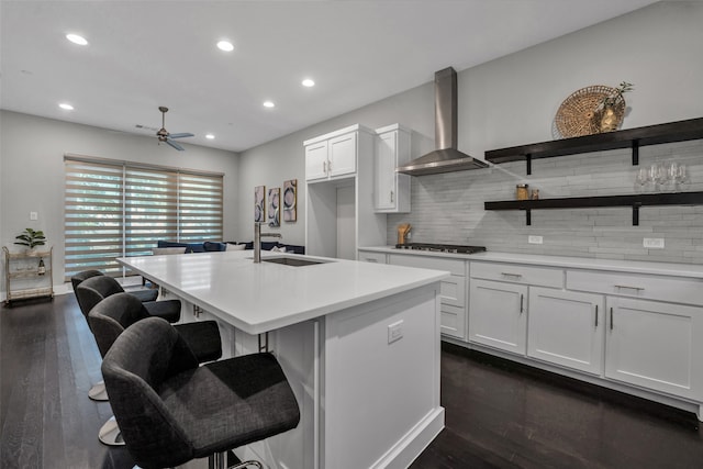 kitchen featuring wall chimney exhaust hood, white cabinets, dark hardwood / wood-style floors, and an island with sink