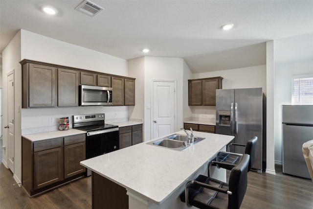 kitchen with sink, an island with sink, dark brown cabinets, dark hardwood / wood-style flooring, and stainless steel appliances