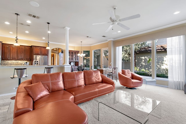 carpeted living area featuring decorative columns, recessed lighting, visible vents, ornamental molding, and ceiling fan with notable chandelier