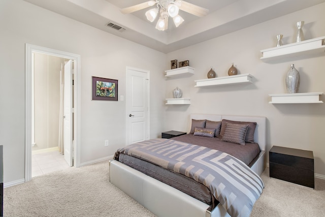 carpeted bedroom featuring a raised ceiling, ceiling fan, and ensuite bathroom