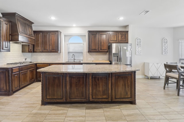 kitchen featuring light stone counters, stainless steel appliances, dark brown cabinets, and a kitchen island