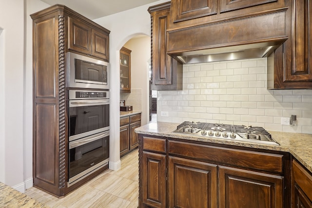 kitchen with appliances with stainless steel finishes, light stone countertops, custom range hood, and backsplash