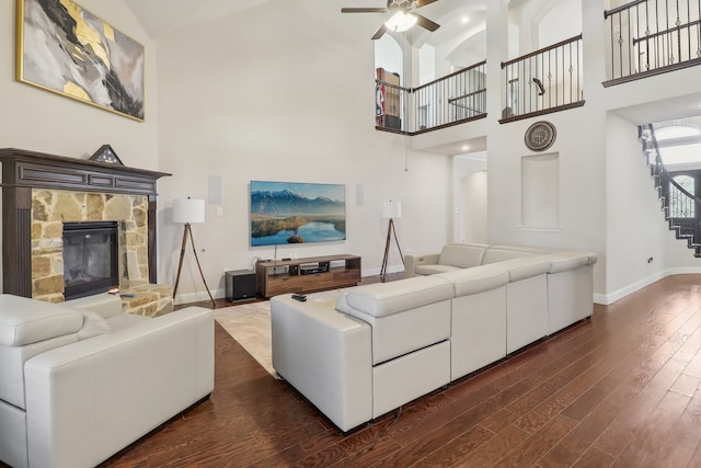 living room featuring a stone fireplace, high vaulted ceiling, dark wood-type flooring, and ceiling fan