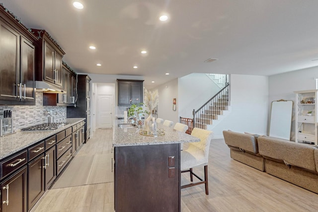 kitchen featuring a center island with sink, sink, light hardwood / wood-style floors, a breakfast bar area, and stainless steel gas cooktop