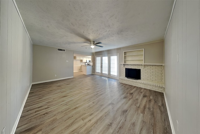 unfurnished living room with french doors, a brick fireplace, a textured ceiling, ceiling fan, and light hardwood / wood-style flooring