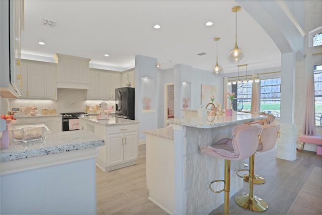 kitchen with light stone countertops, stainless steel appliances, a kitchen island with sink, light hardwood / wood-style flooring, and hanging light fixtures