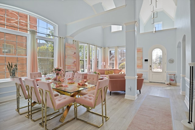 dining area featuring light hardwood / wood-style floors, a towering ceiling, and ornate columns