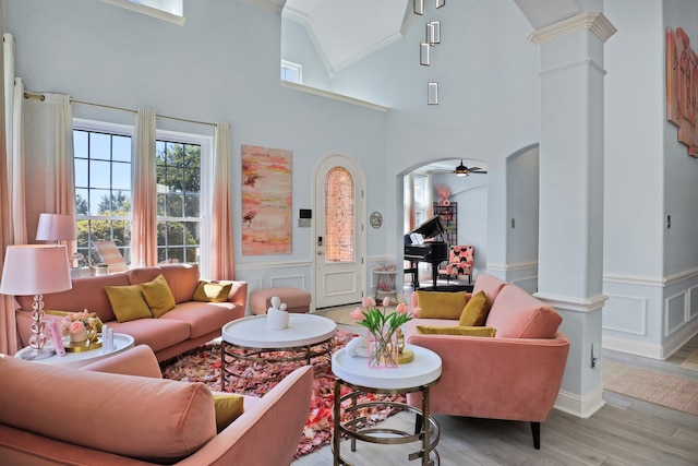 living room featuring high vaulted ceiling, ceiling fan, ornamental molding, light hardwood / wood-style floors, and decorative columns