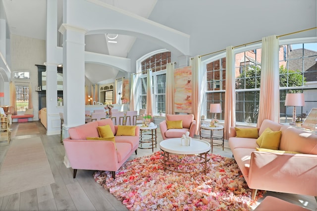 living room featuring light wood-type flooring, high vaulted ceiling, and ornate columns