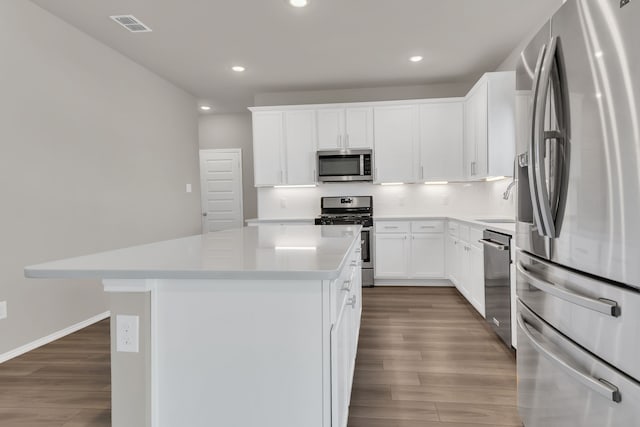 kitchen with a center island, backsplash, hardwood / wood-style flooring, appliances with stainless steel finishes, and white cabinetry