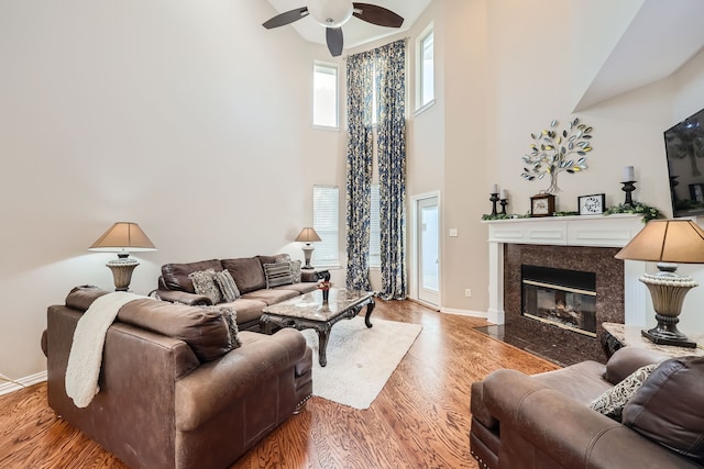 living room with a towering ceiling, a premium fireplace, hardwood / wood-style flooring, and ceiling fan