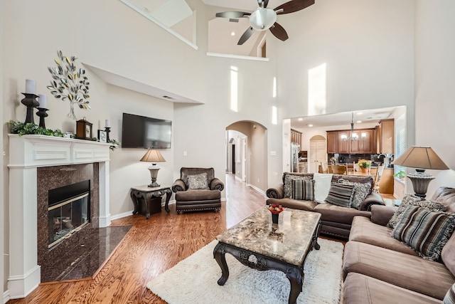 living room with a fireplace, a high ceiling, ceiling fan, and light hardwood / wood-style flooring