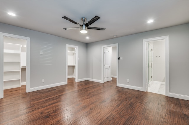 unfurnished bedroom featuring a spacious closet, dark wood-type flooring, ensuite bathroom, and ceiling fan