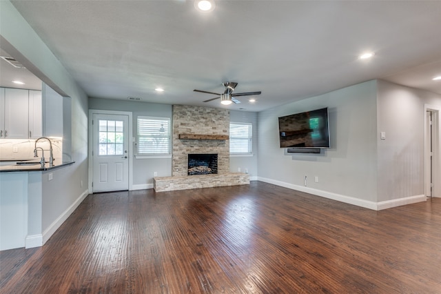 unfurnished living room with sink, dark wood-type flooring, a fireplace, and ceiling fan