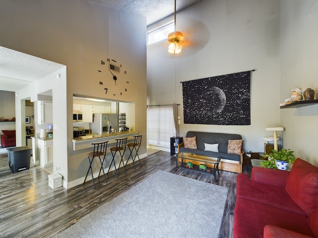 living room featuring ceiling fan, a towering ceiling, a textured ceiling, and wood-type flooring