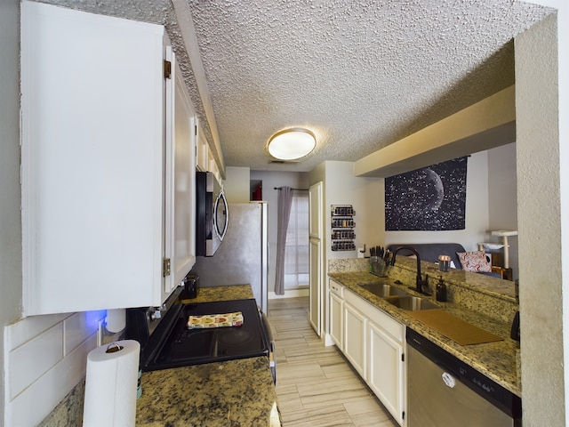 kitchen featuring white cabinets, dark stone countertops, appliances with stainless steel finishes, a textured ceiling, and sink