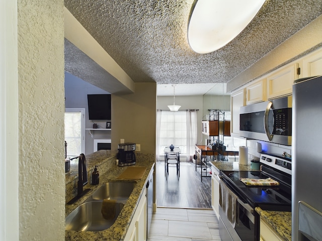 kitchen with stainless steel appliances, dark stone countertops, sink, and hanging light fixtures