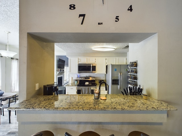 kitchen featuring stainless steel appliances, kitchen peninsula, white cabinets, decorative light fixtures, and backsplash