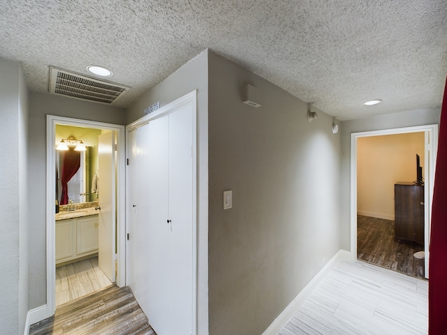 corridor with a textured ceiling, light wood-type flooring, and sink