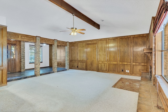 carpeted spare room featuring lofted ceiling with beams, wooden walls, ceiling fan, and decorative columns