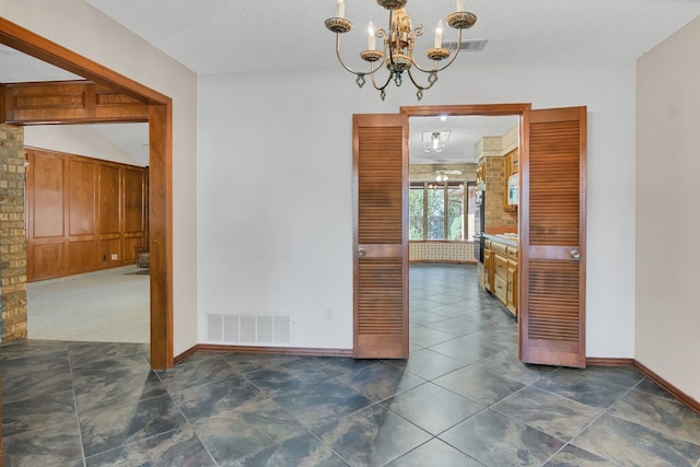 unfurnished dining area with dark tile patterned floors, a textured ceiling, and an inviting chandelier