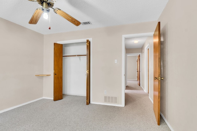 unfurnished bedroom with a textured ceiling, light colored carpet, a closet, and ceiling fan