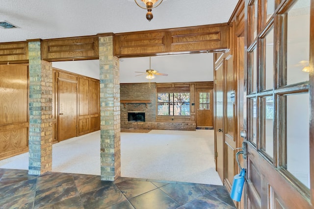 unfurnished living room featuring ceiling fan, a textured ceiling, wooden walls, and dark carpet