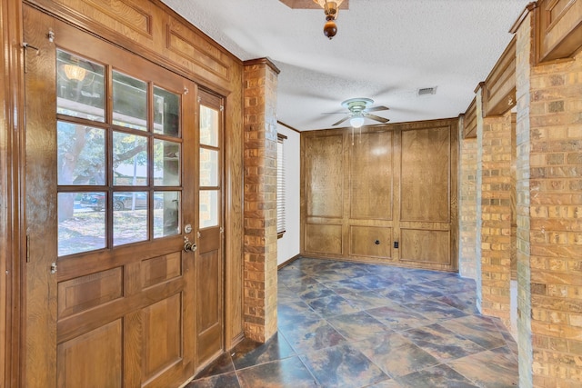 doorway to outside with a wealth of natural light, brick wall, a textured ceiling, and ceiling fan