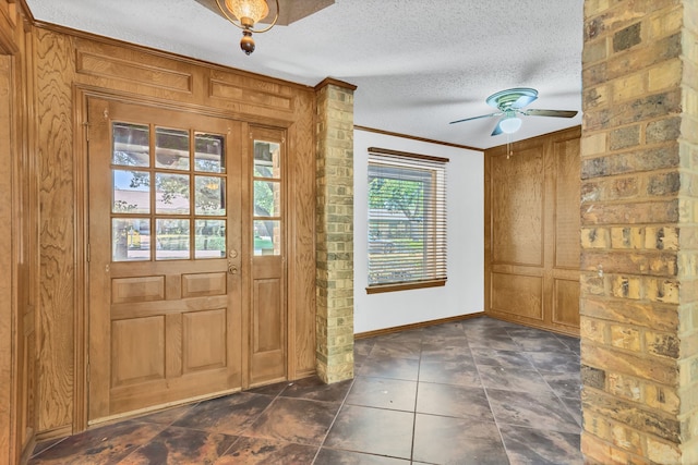 tiled entryway with wooden walls, crown molding, a textured ceiling, and ceiling fan