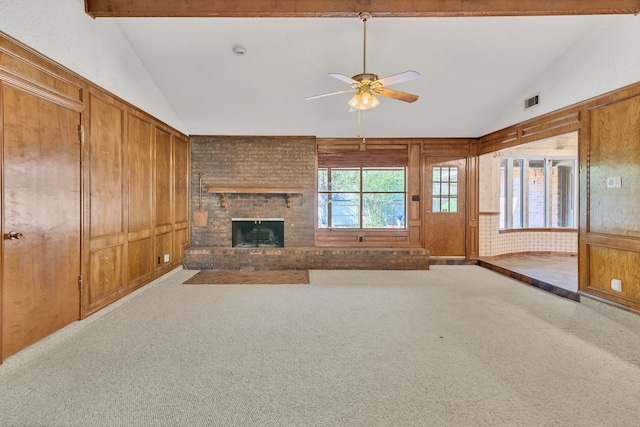 unfurnished living room featuring vaulted ceiling with beams, wooden walls, a brick fireplace, carpet floors, and ceiling fan