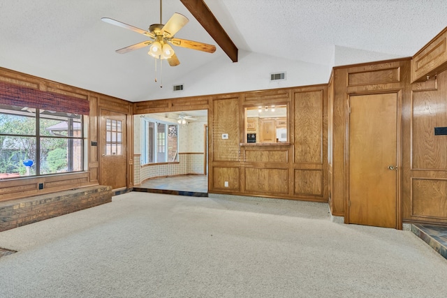 unfurnished living room with lofted ceiling with beams, ceiling fan, light colored carpet, and wood walls