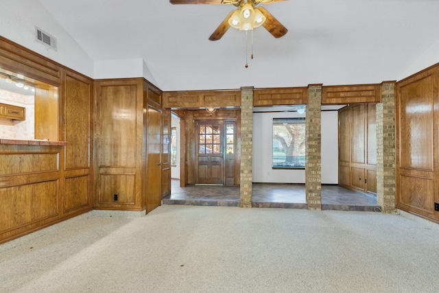 unfurnished living room featuring lofted ceiling, carpet floors, wooden walls, and ornate columns