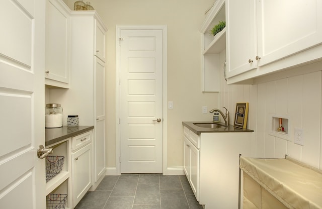 washroom with dark tile patterned floors, sink, washer hookup, and cabinets