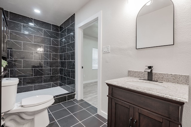 bathroom featuring vanity, toilet, a tile shower, and tile patterned flooring