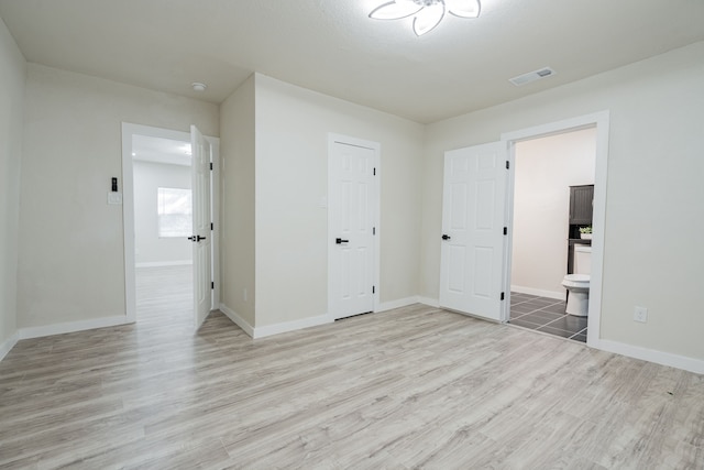 unfurnished bedroom featuring a closet, light hardwood / wood-style flooring, and ensuite bath