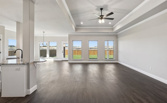 unfurnished living room featuring ornamental molding, ceiling fan with notable chandelier, dark wood-type flooring, and sink